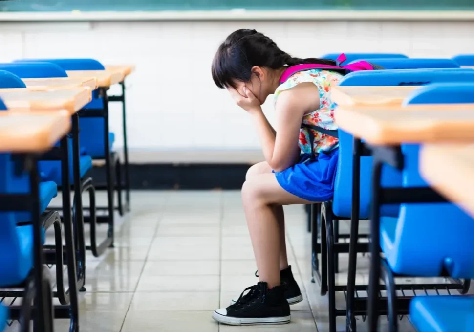 A little girl sitting in front of some desks